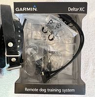 Image of Garmin Delta XC box with charging cable, plastic packaging, and adjustable collar strap with buckle.
