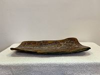 Wide side view of rectangular pottery platter with slightly curved edges on white textured surface.