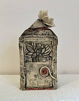 Front view showing carved flower motif with red spiral accent and white flower on vessel roof.