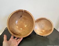 Two handmade turned wooden bowls, one large with natural wood crack and one smaller, held and displayed on stands