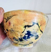 Close up side view of one pottery bowl showing abstract color pattern, held by hand for scale