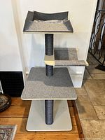 Full view showing the entire multi-level cat bed and scratcher structure with three vertical posts, two lower platforms, and a top cushioned bed.
