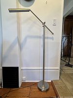 Full view of the modern steel floor lamp showing the adjustable arm and cylindrical light head.