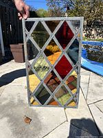 Full view of stained leaded glass window panel held outdoors showing the rectangular shape and diamond pane pattern in various colors including red, yellow, and amber.