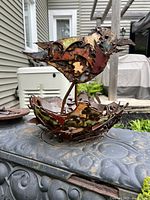 Full view of the steel garden art sculpture showing the songbird standing in the nest on a metal surface outdoors.