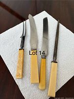 Photo showing all four antique carving utensils: two knives, one two-prong fork, and one sharpening steel with bone handles on a paper towel background.
