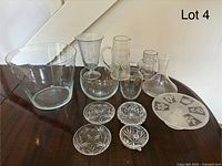 Photo showing collection of 11 assorted clear glassware pieces on a table including punch bowl, goblet, tumblers, vases, and decorative dishes.