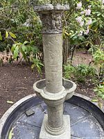 Full side view of cast stone fountain showing column with classical heads, basin, and tub base