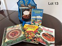 Reusable blue tote bag filled with assorted cookbooks including 'Chutneys & Pickles'. Five main books displayed on table including titles on Greek, Italian, Middle Eastern cooking.