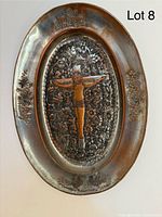Oval metal plaque showing an embossed Jesus figure on the cross with floral and architectural background.