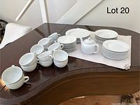 Photo showing the set of over 30 pieces white porcelain dishware arranged on a piano: plates, saucers, cups, and a teapot.
