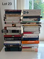 Two stacks of paperback and hardcover books on table against window