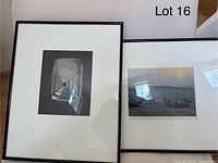 Two framed photographic prints leaning against a wall. Left print depicts arched corridor with shadows, right print shows desert with camels at sunset. Both matted and framed in black minimal frames.