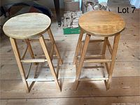 Pair of vintage wooden counter height stools shown from front angle on wooden floor, both with round seats and footrests