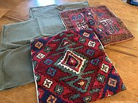 Full set of four cushion covers: two solid olive green canvas-style covers folded, two richly textured hand-embroidered covers with geometric/tribal designs on top