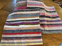 Set of three handwoven cushion covers displayed on wooden table, showing colorful horizontal stripes.
