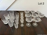 Set of 21 vintage cut crystal glasses arranged on a table separated by type with tumblers on left, liqueur glasses in middle, and coupe glasses on right.