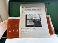 Open green textured case showing 'Econasign Printing Equipment' booklet with stencil sheet in front.