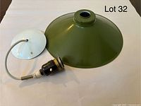 Green enameled metal pendant shade with white interior, vintage ceramic socket, and white ceiling plate shown disassembled on a table.