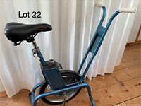 Side view of entire vintage stationary exercise bike showing blue metal frame, curved handlebars with white grips, and black Norco seat