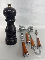 Photo showing dark wooden Peugeot pepper mill with brass knob and four stainless steel bar utensils with light wood handles lying on surface