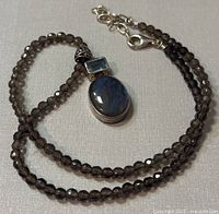 Full view of necklace showing smoky quartz bead chain, silver clasp, and pendant with labradorite and blue topaz stones.