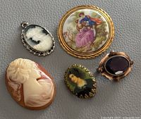 Five antique and vintage brooches and a pendant arranged on gray surface showing all items clearly.
