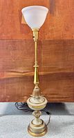 Full view of brass torchiere floor lamp with enameled decorative accents and frosted glass torchiere shade against wood background.