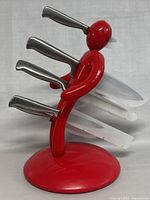 Front view of the red humanoid-shaped knife block with four knives inserted, showing stainless steel handles and plastic blade covers.