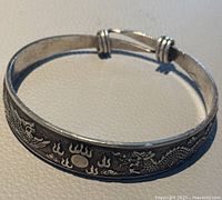Front view of the silver-tone metal bangle featuring engraved dragon and phoenix with flames and a moon symbol.