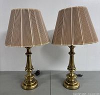 Pair of vintage brass table lamps with beige pleated shades on grey surface.