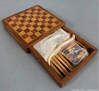 Closed wooden box with chessboard pattern on top and drawer slightly open revealing backgammon pieces in bag.