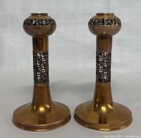 Pair of gilt bronze candleholders with decorative pierced cutouts and wide bases, placed upright side by side.
