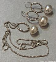 Photo showing silver chain necklace with textured circular pendant and oval white pearl, alongside matching drop earrings.