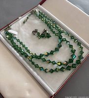 3-strand green bead necklace and matching earrings laid inside a jewelry case.