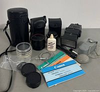 Overview of vintage Canon FD lenses with manuals, lens caps, cases, and cleaning fluid bottle arranged on a flat surface.