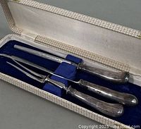 3 piece vintage silver plated carving set in blue velvet lined case with white satin interior, showing knife, fork, and sharpening steel handles.