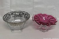 Photo showing both the clear glass bowl with silver floral inlay and the cranberry glass ruffled bowl side by side