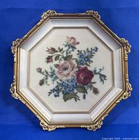 Full view of vintage octagonal framed needlepoint with floral needlework under glass in gold-toned ornate frame.