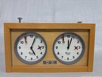 Front view of the vintage wooden GARDE chess clock showing two round analog dials with black and red hands and a natural wood frame.