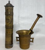 Photo showing the full set: Turkish brass cylindrical grinder next to mortar and pestle on plain background.