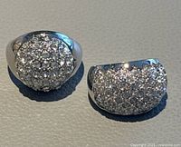 Two white gold plated rings with numerous clear rhinestones on rounded tops, shown side by side on grey surface.