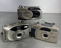 Three vintage Fujifilm 35mm cameras grouped, showing their front faces with lens, flash, and branding.