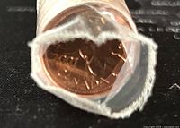 Close-up image showing the open end of the paper roll containing the Canadian 1 cent coins, the front coin visible with the year 2001 and maple leaf design.