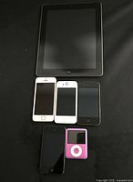 Apple lot including iPad, three iPhones, and two iPods, all powered off, on black surface