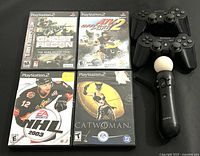 Photo showing 4 PlayStation 2 game cases: Tom Clancy's Ghost Recon, ATV Offroad Fury 2, NHL 2003, and Catwoman, plus 3 Sony controllers on a black surface.