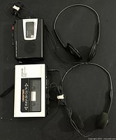 Top-down view of black Sony Walkman WM-FX191 cassette player with silver cassette door. Includes black wired headphones with headphone band extended.