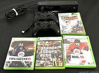 Photo showing two black Xbox controllers, Kinect sensor, and four Xbox 360 game cases (FIFA Soccer 10, Grand Theft Auto IV, NHL 10, Rayman Origins).