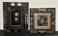 Two African masks displayed in carved shadow box frames side by side on a white wall