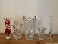 Front view of all five crystal vases arranged in a line on a wooden surface.